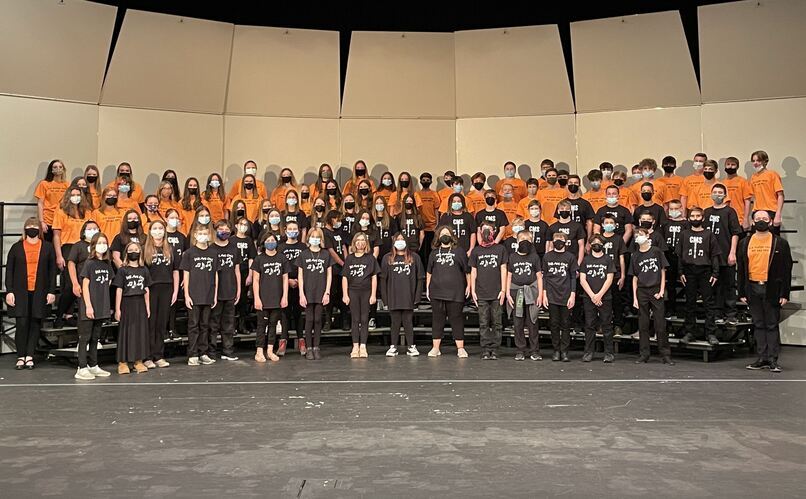 groups of choir students in orange and black shirts standing on a set of risers